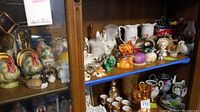 Overview of shelf with collection of decorative ceramic and glass figurines, pitchers, and vases.