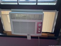 Front view of GE window air conditioner installed in window, showing full unit and vent design