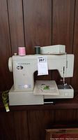 Vintage beige Kenmore sewing machine with two thread spools and floral stitched plate visible.