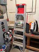 Full view of one aluminum Davidson A-frame ladder with red top cap and six steps, showing scratches and use in a workshop with tools around.