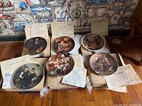 Six collector plates laid out on floor with accompanying Certificates of Authenticity and cardboard packaging visible around them.