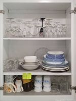 Overview of entire collection showing stemware, mugs, bowls, and dishes in cabinet shelves.