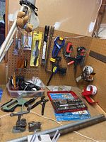 Photo showing several clamps mounted on pegboard, socket set case on bench, staple gun, and various loose hand tools in containers.