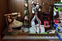 Wide view of lot showing vintage-style landline phone, tall decorative vase with female face, modern metallic vase with white flowers, small decorative pitchers, and glass containers.