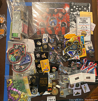 Photo showing a variety of patches, pins, and memorabilia spread over a surface, including multiple space mission patches and assorted collector pins on cards or in plastic.