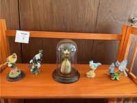 Photo showing five bird statues with a brass pineapple in a glass dome on wooden shelf