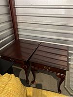 Two dark wood cherry end tables placed side by side showing curved legs and drawer fronts with brass handles.