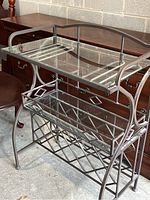 Photo showing angled side view of the metal framed glass display shelf with two levels, highlighting the top glass shelf and lower basket shelf with decorative metal frame