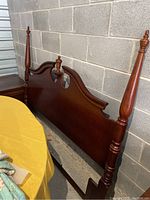 Full view of the wooden full-size bed headboard showing the left side post and the carved top edge.