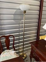 Full view of the standing floor lamp showing its tall metal pole, stained base, and white inverted bowl-shaped shade on top.