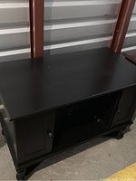 Front angle showing the top, doors, and side panels of the black lacquered wood TV stand