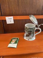 Photo showing the full view of the vintage Kaiser Porzellan beer stein with metal lid and a small booklet tag next to it.