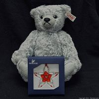 Grey mohair Steiff teddy bear sitting upright with Swarovski crystal poinsettia star ornament box placed in front.