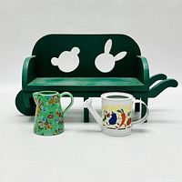Front view of the lot showing the green wooden wheelbarrow bench, floral green watering can and colorful white watering can