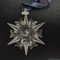 Swarovski crystal star-shaped Christmas ornament with metal 2002 tag and hanging ribbon against black background.