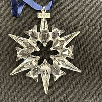Close-up front view of clear Swarovski crystal star ornament with 2007 tag and blue ribbon on dark fabric background