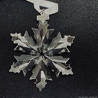 Close-up of the clear faceted Swarovski crystal snowflake star ornament with a white hanging ribbon and a small 2014 metal year tag.