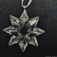 Close-up of the clear multifaceted Swarovski crystal star ornament showing the faceted design and white hanging ribbon on a black background.