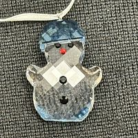 Close-up of Swarovski crystal snowman ornament with blue hat and red nose on a gray fabric background.