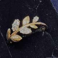 Close-up image of gold-tone ring with clear marquise-cut Swarovski crystals and leaf details on a black display.