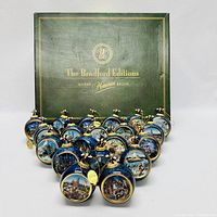 Photo showing 18 Bradford Editions Disney ornaments with blue marbled background, gold rims, Disney scenes, and Mickey Mouse figure tops arranged in front of green edition box.