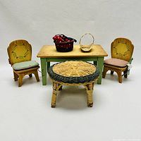 Front view of the miniature furniture set showing two decorated wooden chairs with cushions, green table, round wicker stool, and two small baskets.