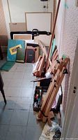 View of room corner with multiple wooden easels, portfolios, record books and boards leaning against wall.