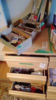 Overview of multiple boxes and wooden drawers containing craft supplies, bindings, rulers and other sewing tools.