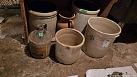 Full set of glass jug and various sizes of stoneware crocks arranged on floor.