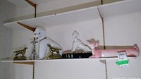 Shelf with large white poodle figurine, pink dachshund-shaped dish ashtray, and pair of brass Irish setter bookends.