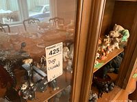 Wooden shelf displaying 30 assorted dog figurines with a MaxSold sticker noting one cracked item.