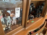 Wide view of multiple dog figurines in wooden cabinet showing variety and sizes.