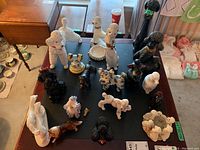 Overview of all 18 dog figurines varying in size, color, and breed representation on black mat on wood table.