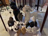 Wide view showing all statues including black ceramic poodle, white ceramic lamp poodle, metal wireframe poodle, composite poodles in tan, black, and white, dark metal abstract dog, and wooden rabbit statue.