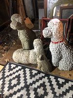 Four off-white ornamental poodle dog statues grouped on a garage floor with varied sizes and detailed curly fur textures.