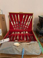 Full view of wood storage box showing 20 flatware pieces arranged in red velvet compartments and a gray rolled storage pouch with additional flatware pieces in front.
