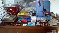 Wide view showing two jewellery boxes, plastic barrettes, assorted pins including Mickey Mouse, buttons, earrings and small packaged items on a table.