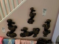 Four black and gold decorative poodle plaques mounted on a white wall showing their different sizes and poses, ranging 10-14 inches tall.