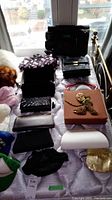 Photo of 10 assorted evening bags and clutches displayed on a bed near a window, showing various colors and materials including black, pink, and patterned bags