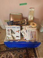 Full view of blue plastic bin filled with sewing pattern envelopes including Kwik Sew and McCall's, and sewing supplies like rotary cutter, rulers, scissors, and pattern tracing paper roll.