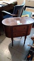 Full view of closed wooden sewing cabinet showing oval top, drawer, and turned legs.