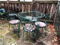 Full view of the round glass top metal table and four matching chairs placed outdoors on stone patio.