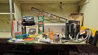 Wide view showing assortment of tools on a shelf including metal level, clamps, screwdrivers, toolbox, and hand tools.