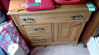 Wood wash stand with three drawers and a storage door, showing metal handles and natural wood finish with some personal items on and around.