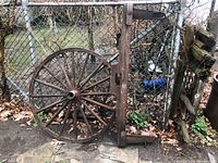 Front view of metal-rimmed wooden wagon wheel and weathered wooden yoke leaning against a chain link fence