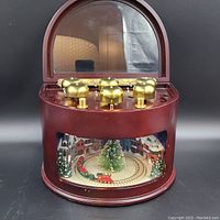 Front view of the animated symphony of bells train with visible brass bells on top and winter village scene inside under clear panel.