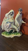 Full view of the porcelain nativity scene showing Mary holding baby Jesus next to Joseph and a sheep on a decorative base.