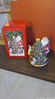 Photo showing the cookie jar alongside its original decorated box, depicting Santa trimming a Christmas tree.