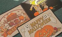 Close-up of three seasonal welcome mats showing fall harvest pumpkins, scarecrow, and Halloween jack-o'-lantern with ghosts.