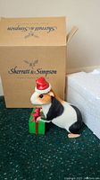 Country Artists guinea pig Santa figurine holding a green and red gift box with Sherratt & Simpson box behind it.